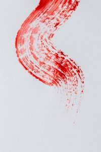 Abstract red paint stroke on white background, capturing dynamic brush movement.